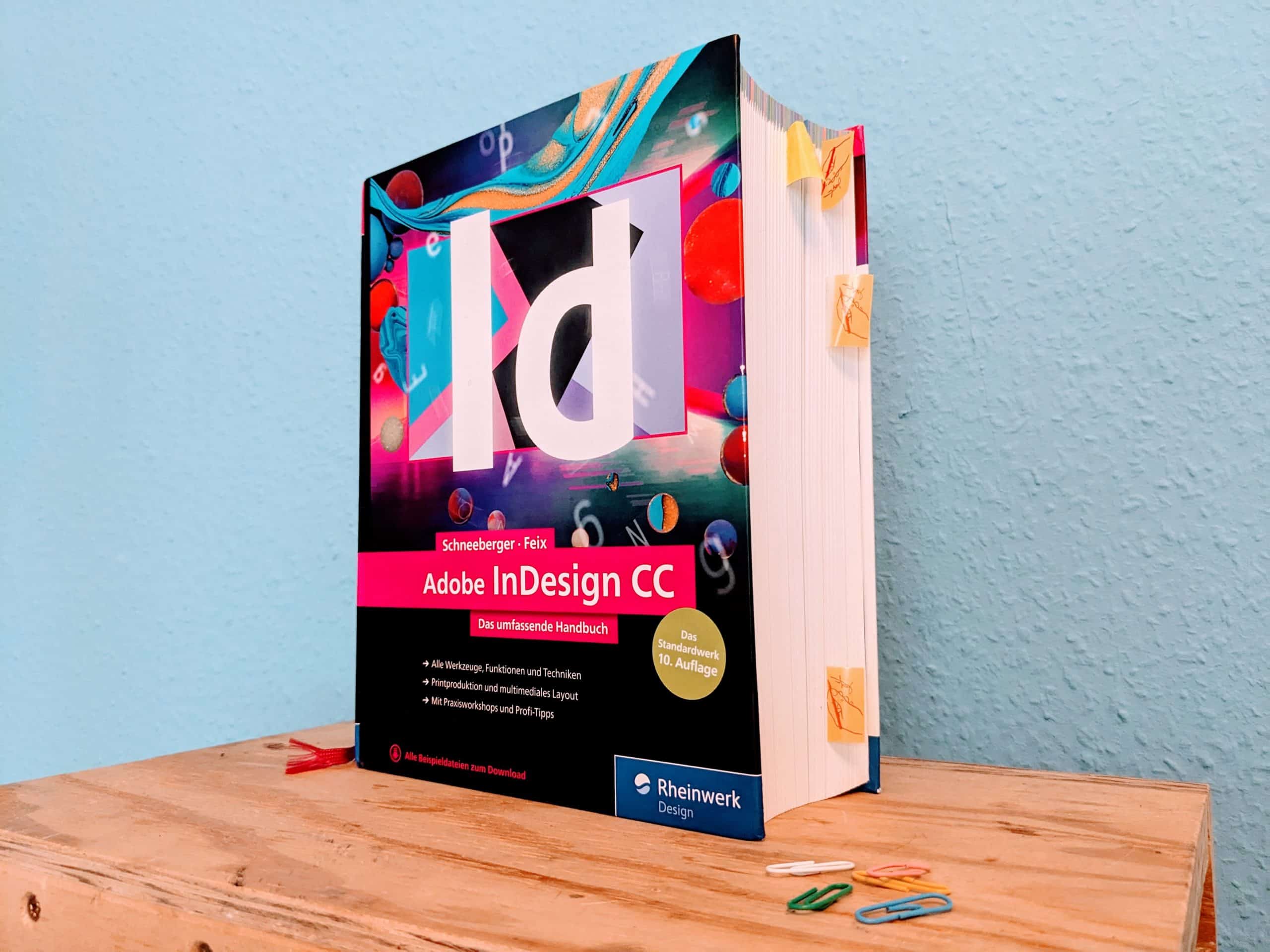 Fotografie des Buchs Adobe InDesign CC, das umfassende Handbuch vor blauem Hintergrund
