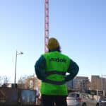 Mitarbeiterin der Firma midok® steht bekleidet mit Schutzhelm und Warnweste vor einer Baustelle mit rotem Kran.