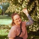 Anna, Mitarbeiterin von midok, steht vor einem blühenden grpßen Busch und lächelt in die Kamera.