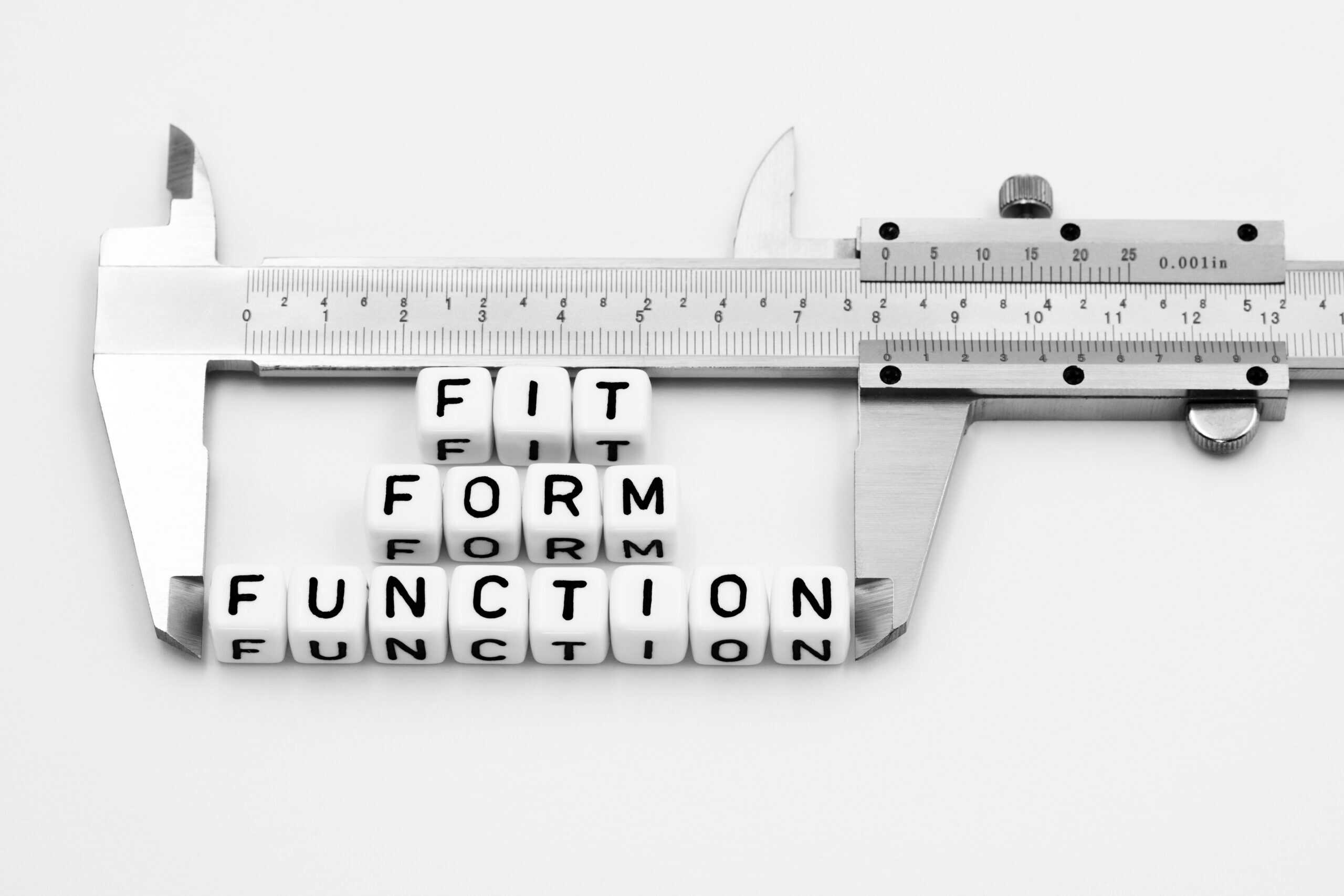 Auf einem weißen Tisch liegt ein Messchieber. Zwischen seinen Messflächen liegen kleine Buchstabenwürfel mit den 3 Worten Fit, Form und Function