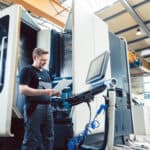 Ein Arbeiter steht vor einer großen Maschine und hält einen Zettel in der Hand